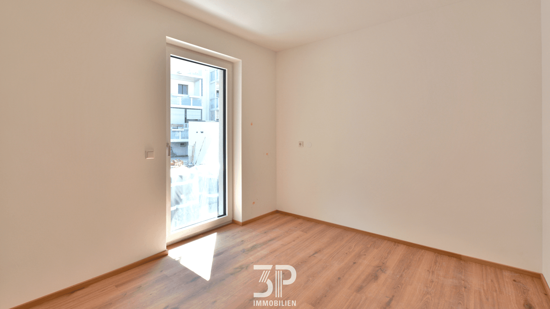 Helles Schlafzimmer mit Laminatboden und Zugang zu einem Balkon oder einer Terrasse.