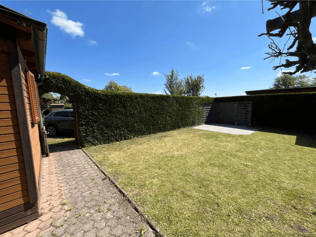 Weitläufiger Garten mit Rasen, gepflastertem Weg und hoher Hecke, die Privatsphäre bietet.