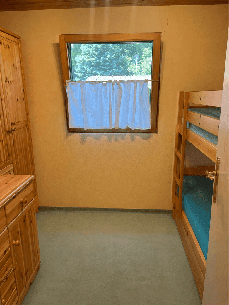 Kinderzimmer mit Etagenbett, Holzschrank und Fenster mit Blick ins Grüne.