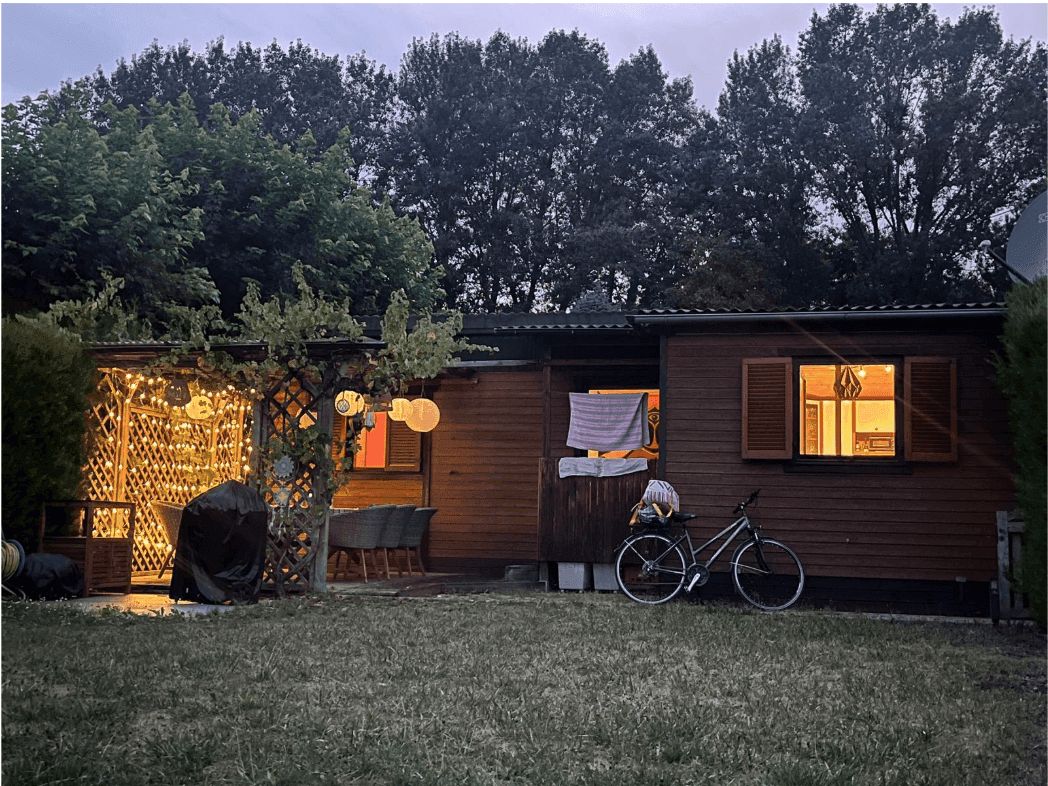 Gemütlicher Gartenbereich am Abend mit beleuchteter Terrasse und Holzhaus, umgeben von Bäumen.