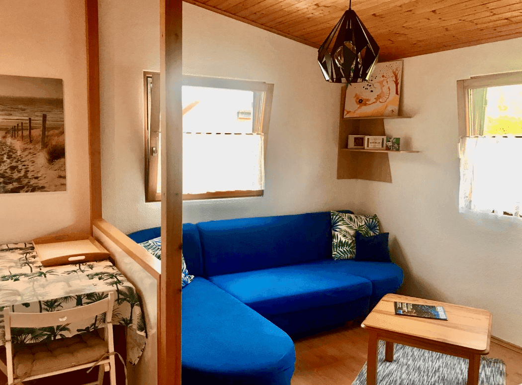 Heller Wohnbereich mit blauer Eckcouch, Holzbalkendecke und kleinem Couchtisch.