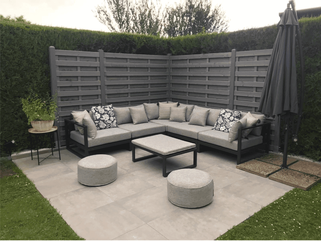 Moderne Lounge-Terrasse mit bequemen Sofas, Couchtisch und Sonnenschirm, umgeben von Hecken.