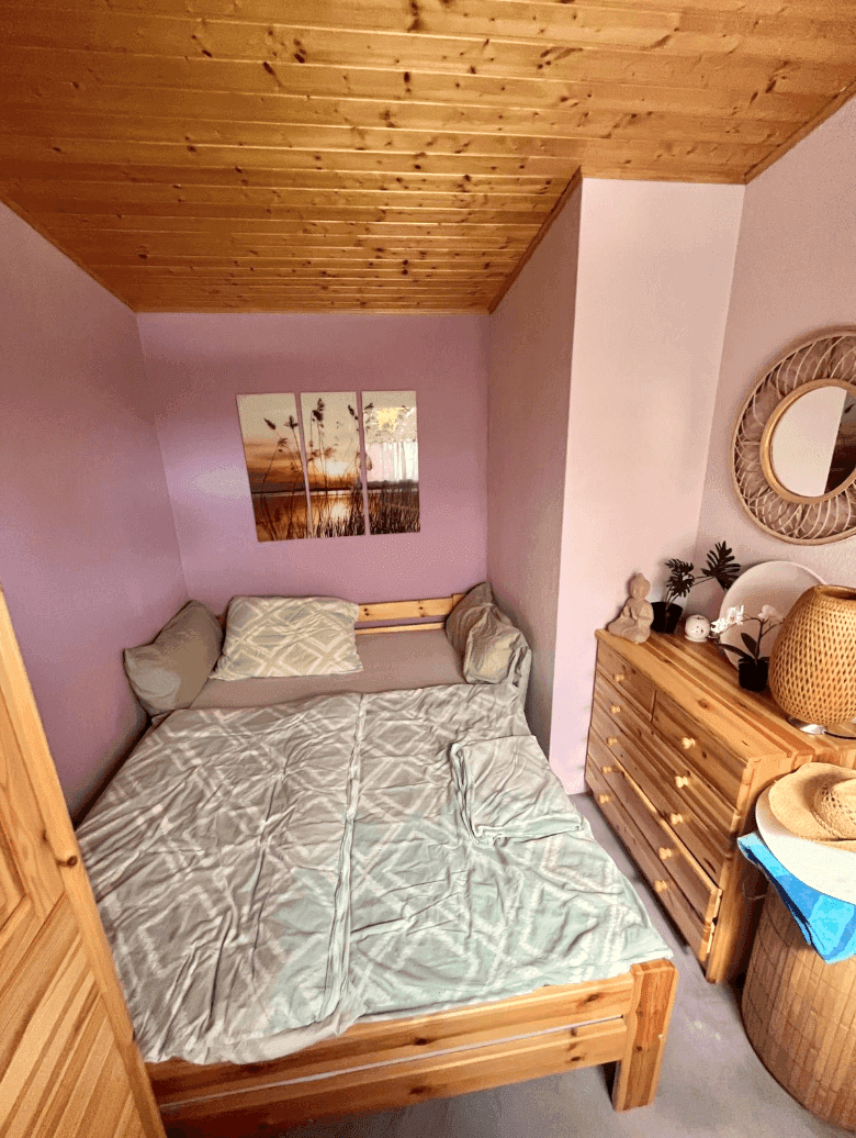 Gemütliches Schlafzimmer mit Holzbett, Kommode und lila Wänden unter einer Holzdecke.