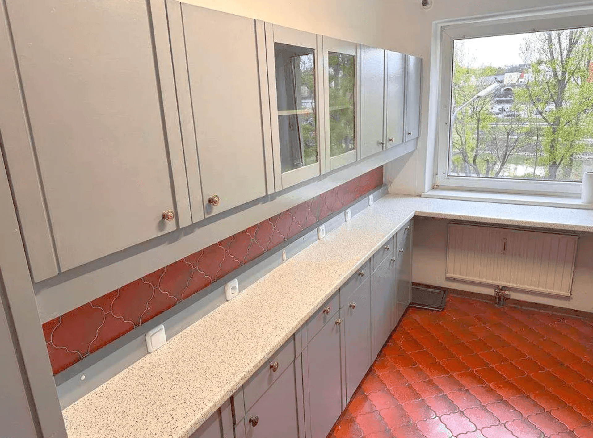 Funktionale Küche mit grauen Oberschränken, viel Arbeitsfläche und Fenster.