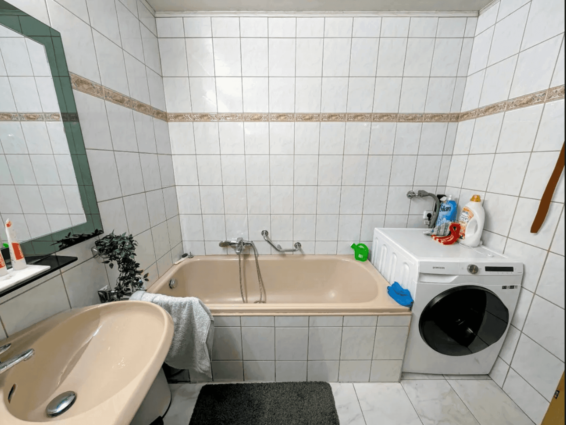 Badezimmer mit Badewanne, Waschbecken und Waschmaschine, gefliest in hellem Design.