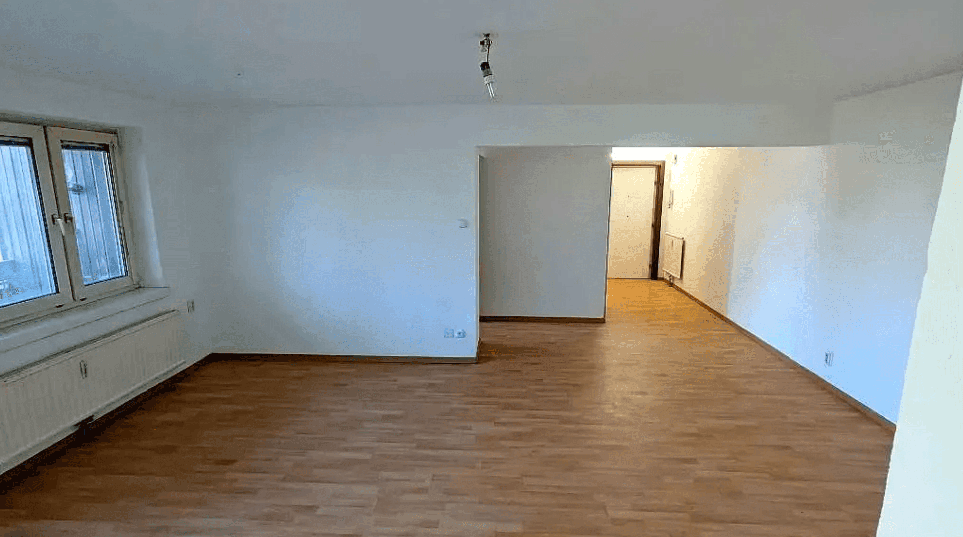 Geräumiges, unmöbliertes Zimmer mit Holzboden und Blick auf den Eingangsbereich.
