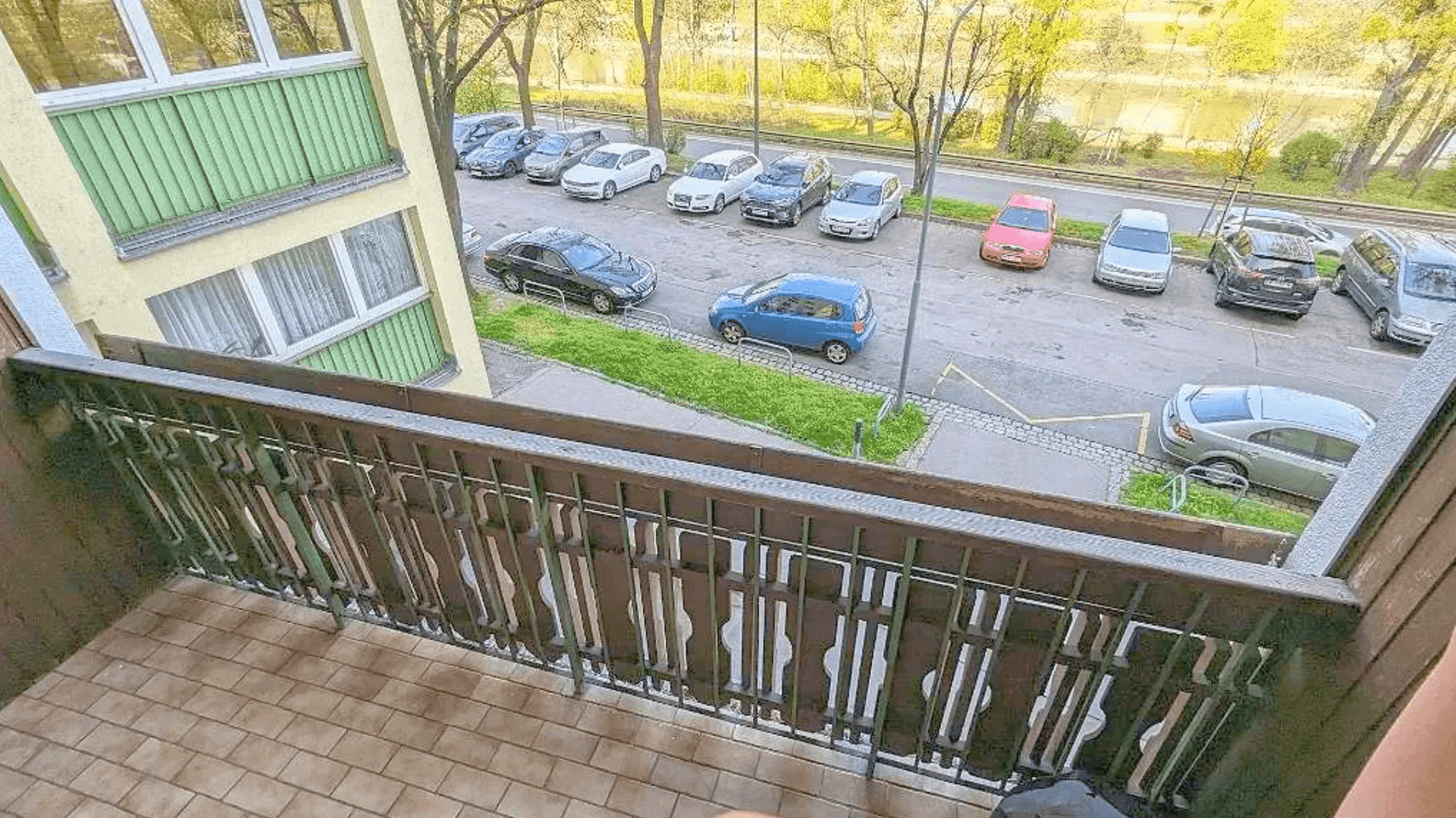 Blick vom Balkon auf die Straße, den Fluss und die umliegende Grünfläche mit parkenden Autos.
