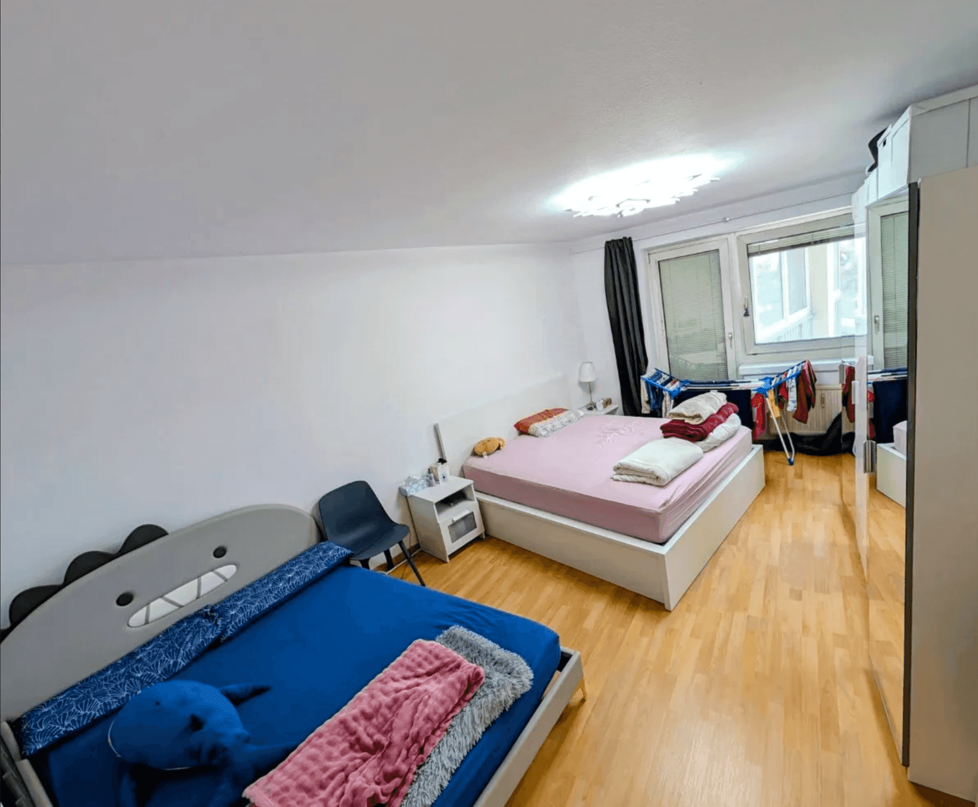 Helles Schlafzimmer mit zwei Betten und Holzboden, bietet Platz für mehrere Personen.