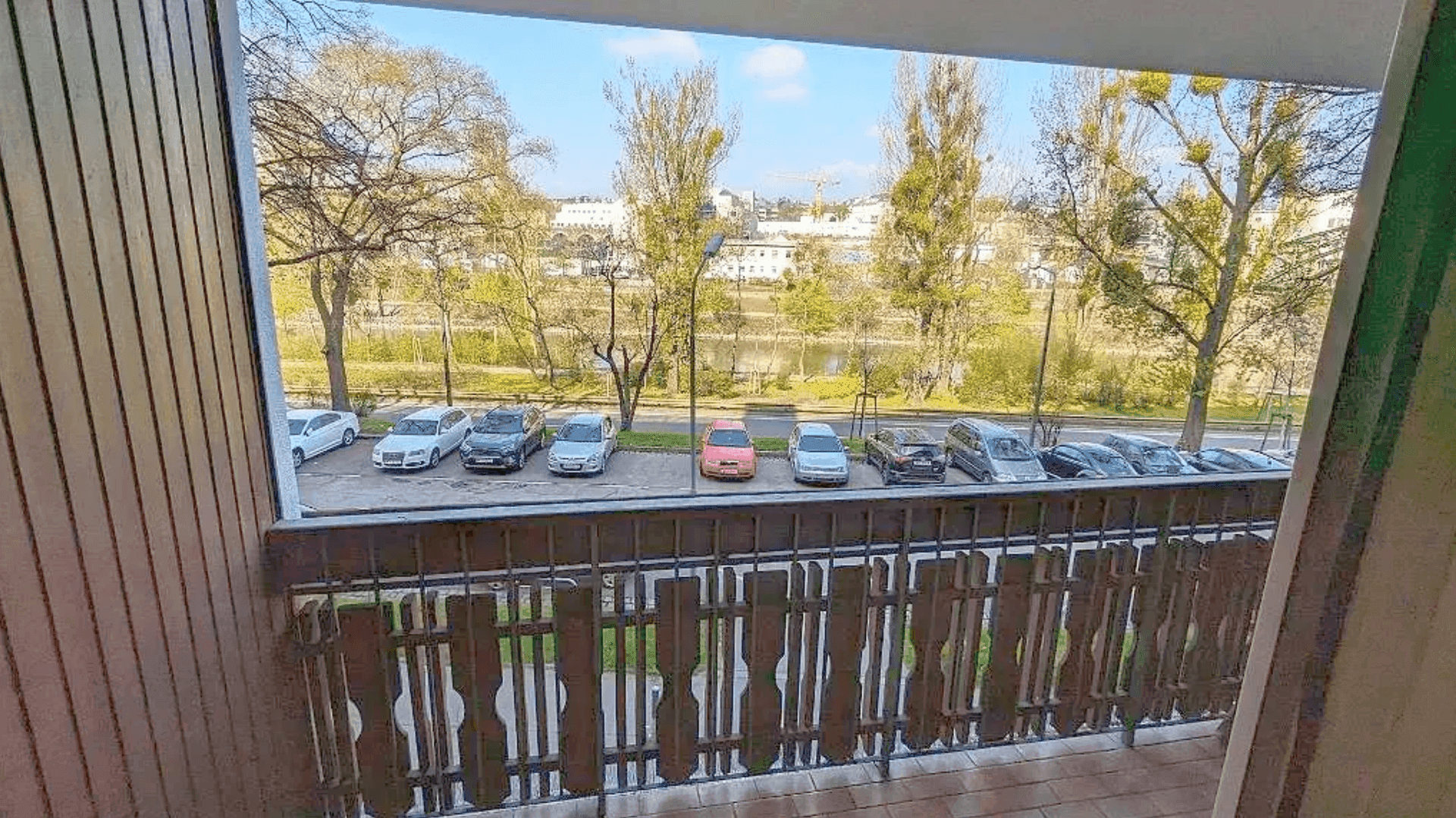 Balkon mit Blick auf die Straße, parkende Autos und einen Fluss im Hintergrund.