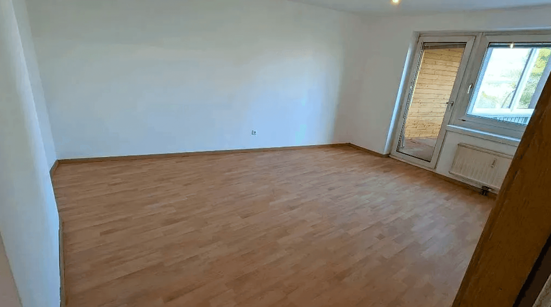 Leeres Zimmer mit Holzboden und direktem Zugang zu einem Balkon oder einer Loggia.