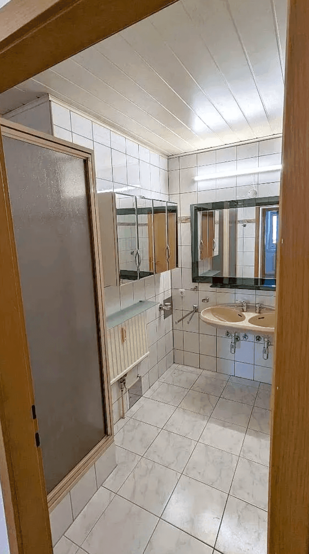 Badezimmer mit Duschkabine, Doppelwaschbecken und Spiegelschrank, gefliest in hellem Design.