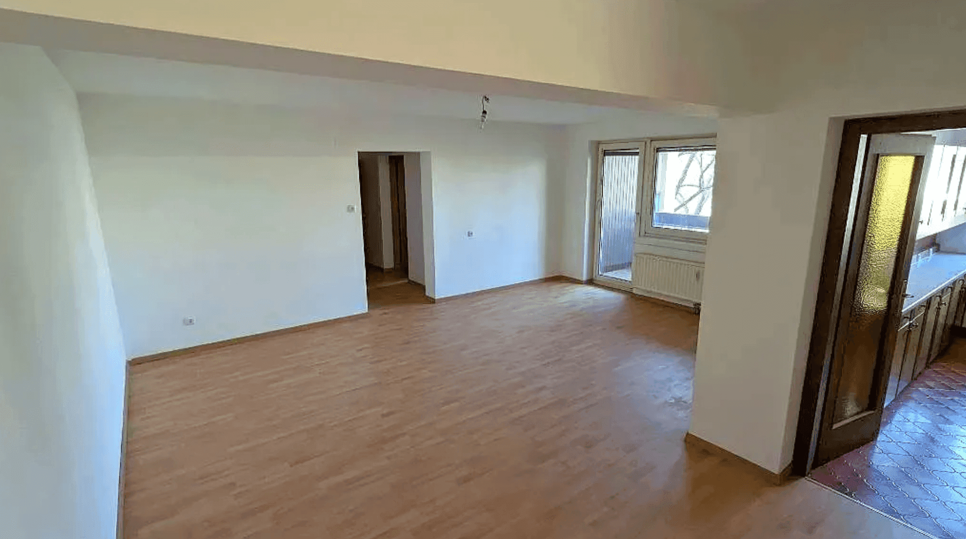 Heller, unmöblierter Wohnbereich mit Holzboden und Zugang zu Balkon und Küche.