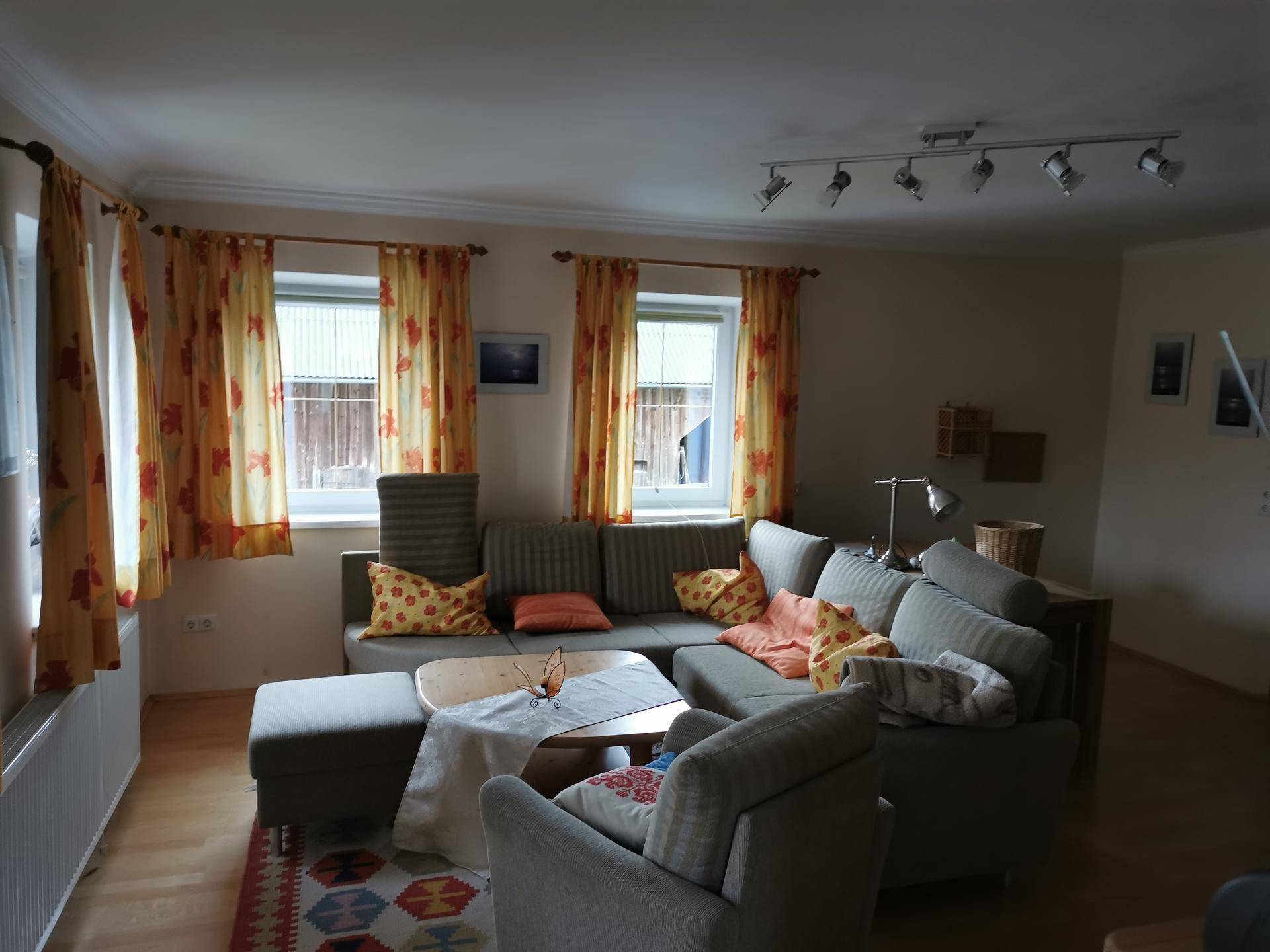 Gemütliches Wohnzimmer mit großem Ecksofa, Holzboden und farbenfrohen Vorhängen.