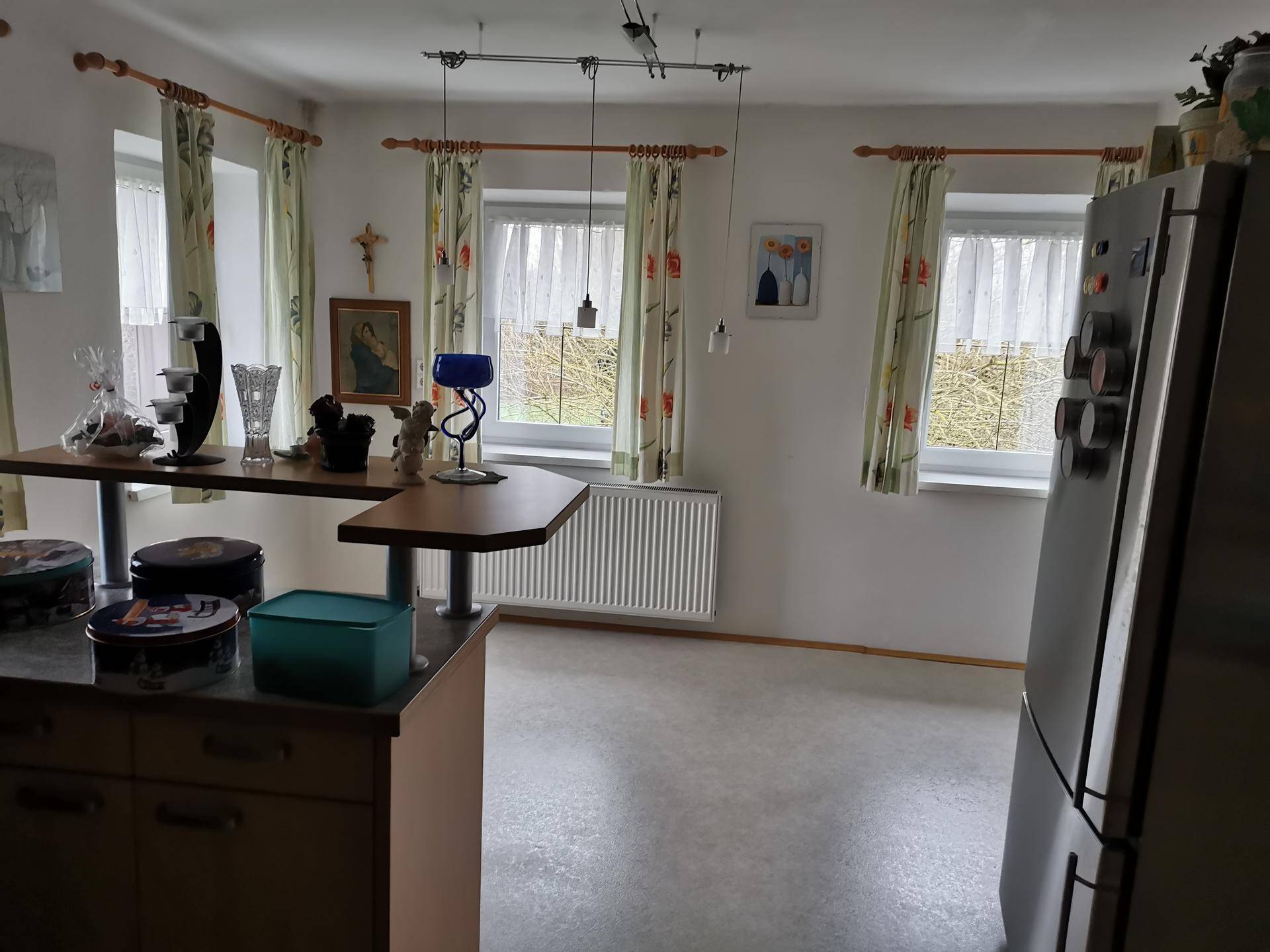 Heller Küchenbereich mit Frühstückstheke und Blick ins Grüne durch mehrere Fenster.