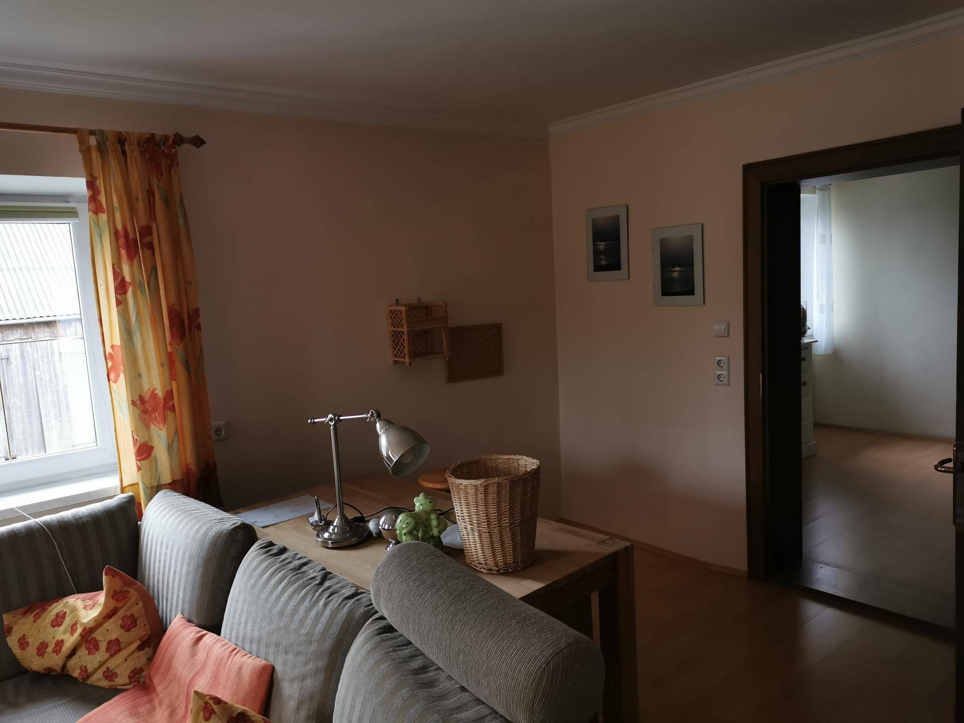 Wohnzimmer mit beigem Sofa, Holzboden und offenem Durchgang zu einem weiteren Raum.