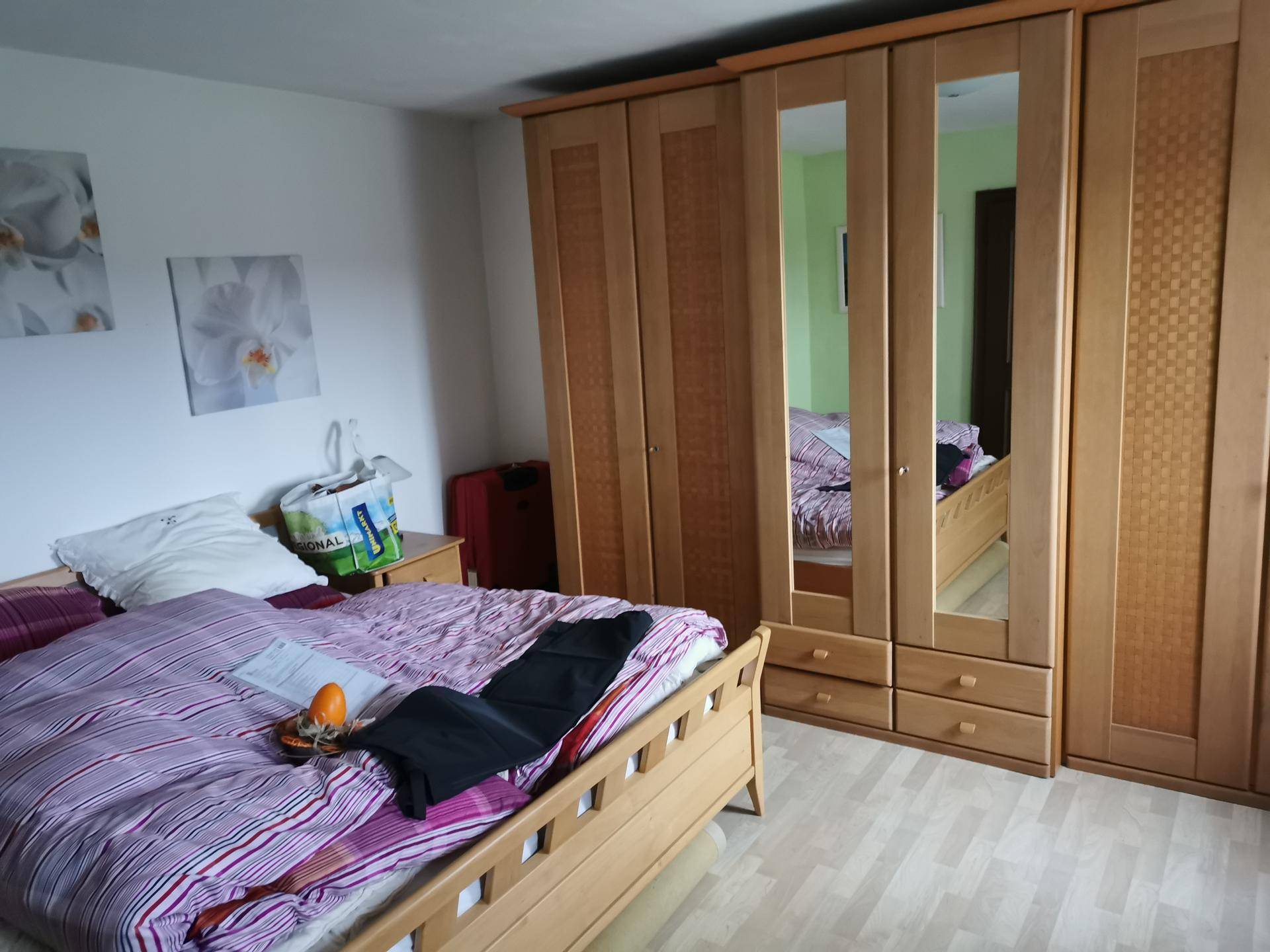 Schlafzimmer mit hellem Holzbett, großem Spiegelschrank und Laminatboden.