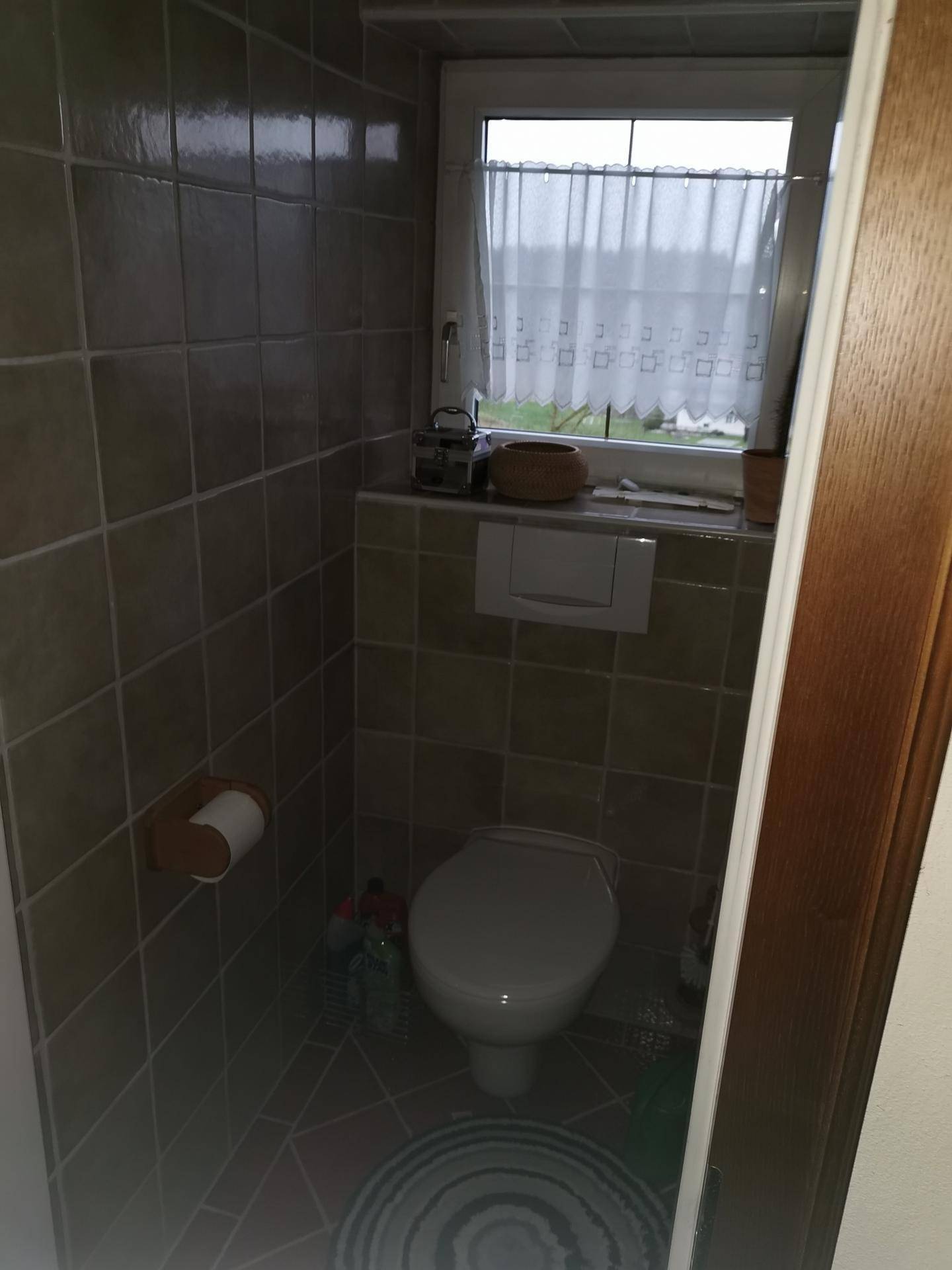 Separate Toilette mit Fliesenboden und einem Fenster für natürliche Belüftung.