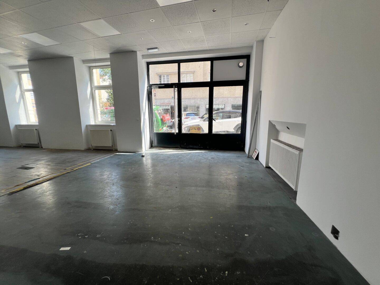 Ladenfläche mit großem Schaufenster und Betonboden, bereit für den Ausbau und die Gestaltung.