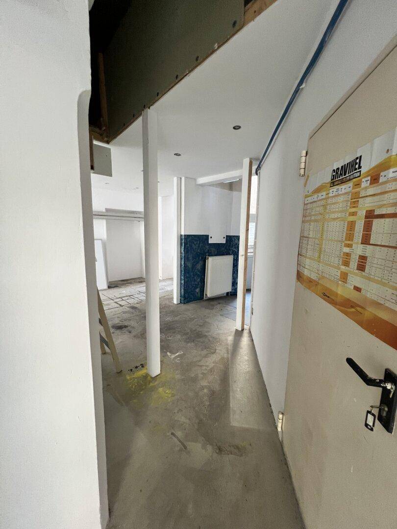 Flur in einem Gebäude, der zu weiteren Räumen führt, mit sichtbaren Bauarbeiten und Betonboden.