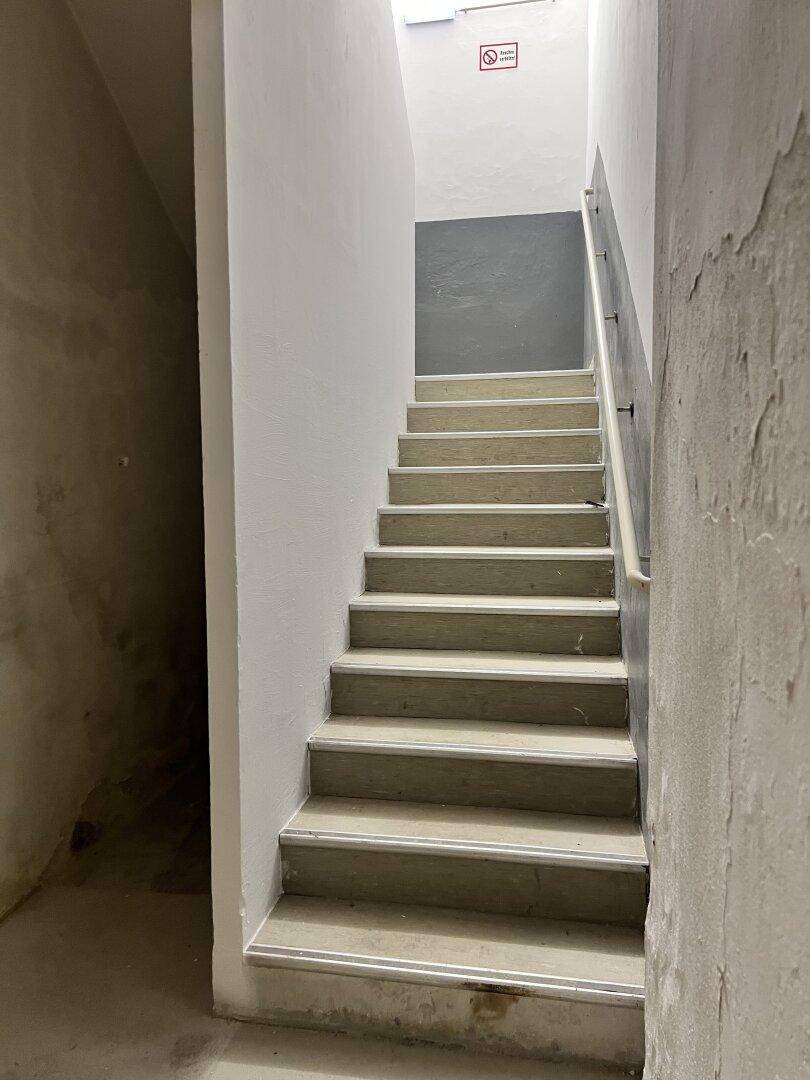 Treppenhaus mit Betonstufen und Handlauf, das in ein höheres Stockwerk führt, schlicht.