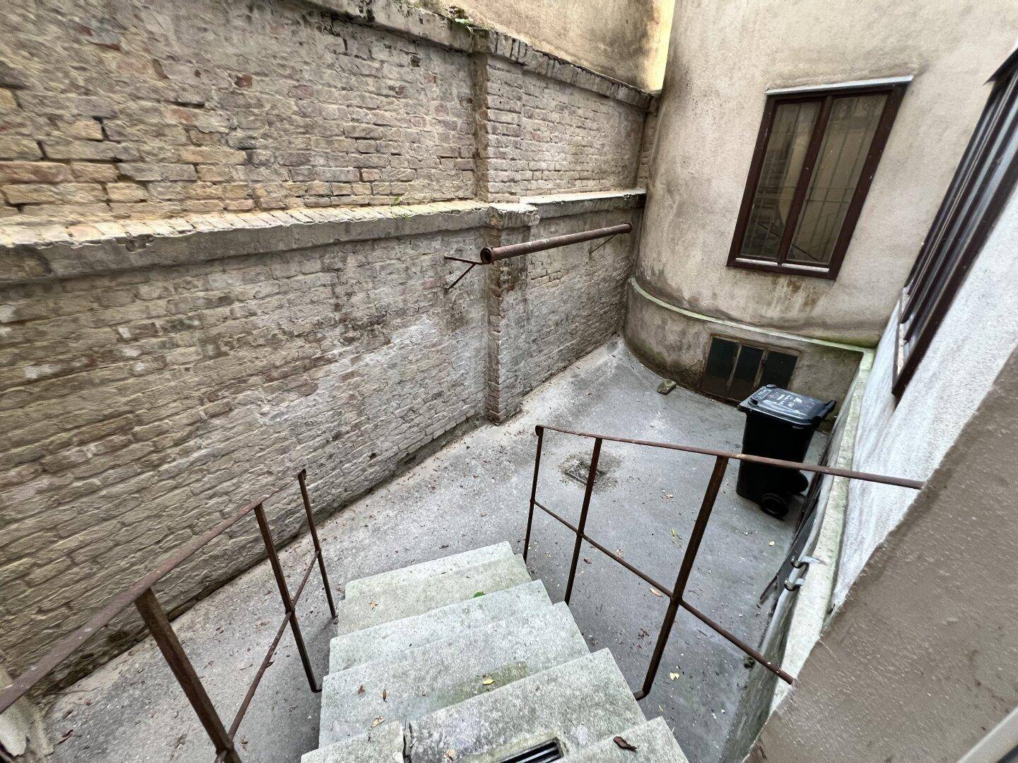 Kleiner, ummauerter Innenhof mit Treppe und Mülltonnen, umgeben von Backsteinwänden, funktional.