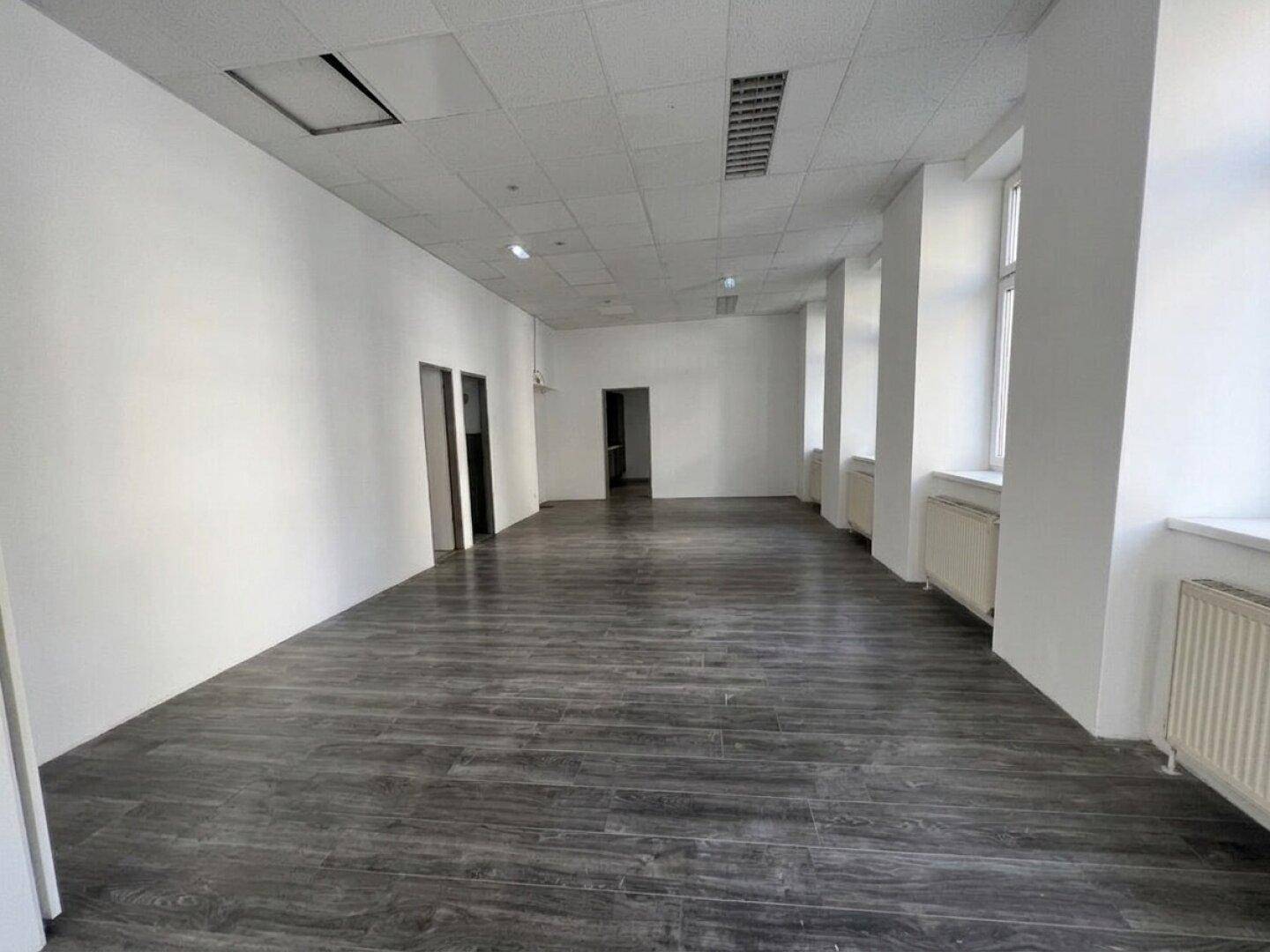 Geräumiger Büroraum mit dunklem Laminatboden und mehreren Fenstern, bietet viel Platz.