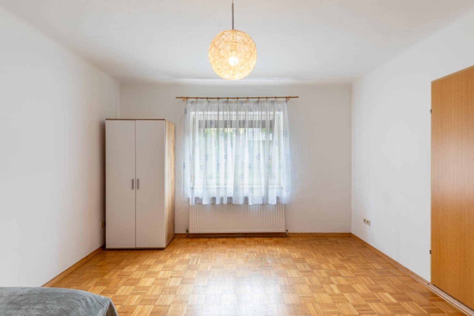 Helles Zimmer mit Parkettboden und großem Fenster, ausgestattet mit einem Kleiderschrank.