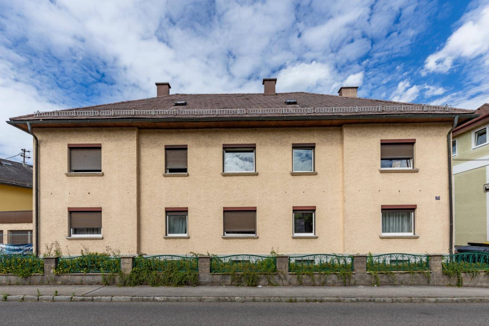 Traditionelles Mehrfamilienhaus mit beiger Fassade und braunen Fensterläden an einer Straße.