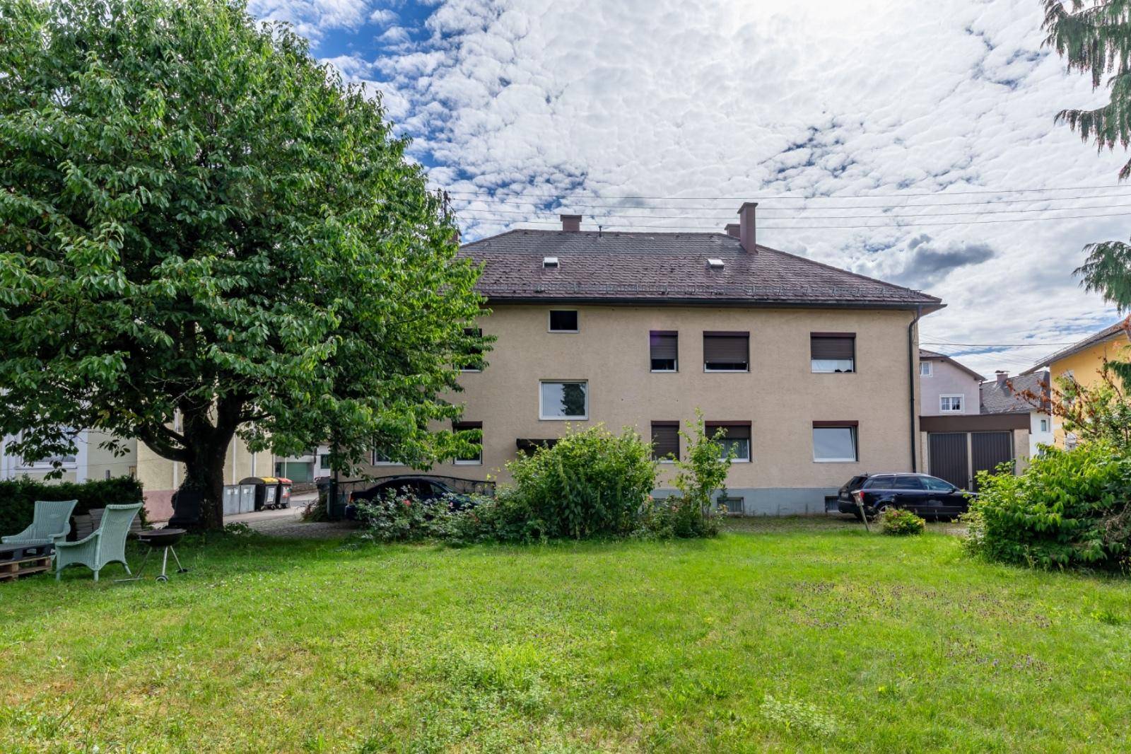 Großer Garten hinter dem Haus mit Rasenfläche, Bäumen und einer kleinen Sitzecke.