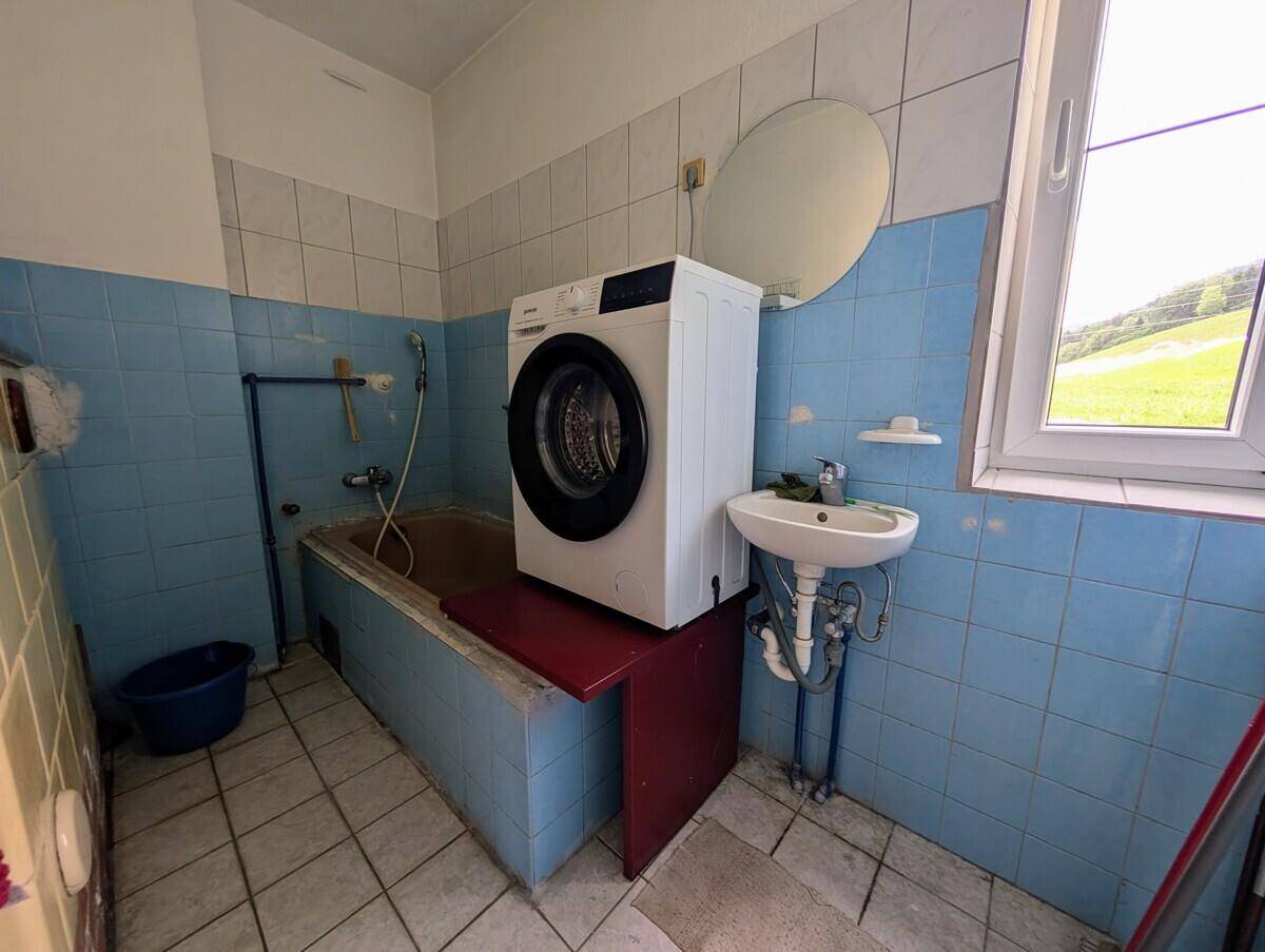 Badezimmer mit blauen Fliesen, Waschbecken, Badewanne und Fenster, im Stil der 80er Jahre.