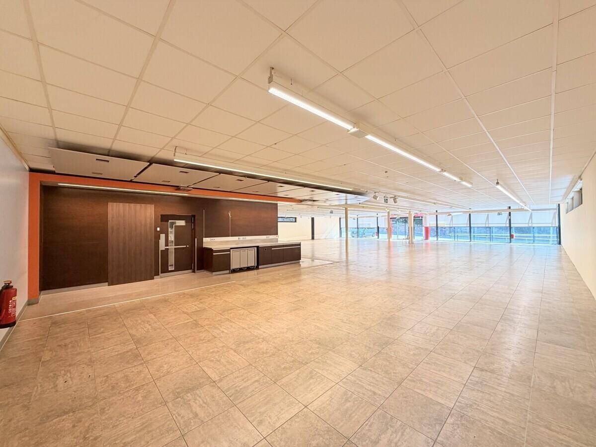 Großer, offener Gewerberaum mit Fliesenboden, abgehängter Decke und einer Theke im Hintergrund, bereit zur Nutzung.