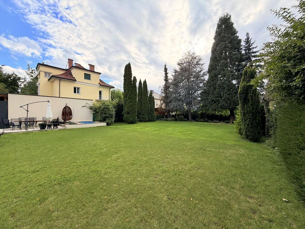 Großer Garten mit weitläufigem Rasen, umgeben von Bäumen und Hecken, mit Blick auf das traditionelle Haus.