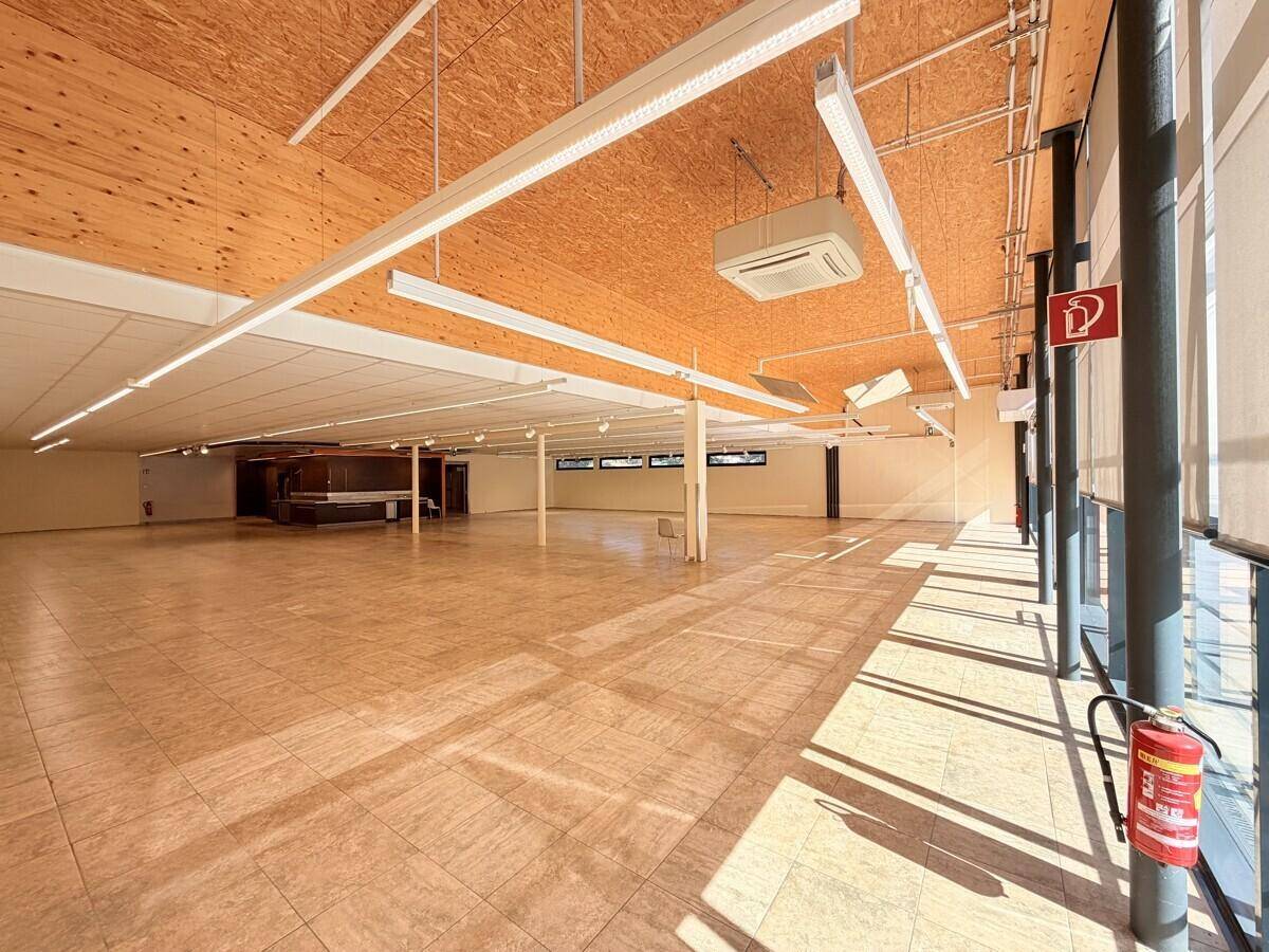 Weitläufiger Gewerberaum mit Holzdach, Fliesenboden und großen Fenstern, die viel Tageslicht hereinlassen.
