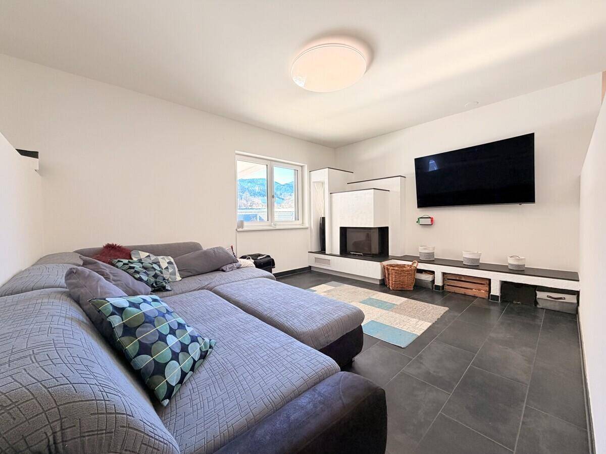 Gemütliches Wohnzimmer mit großem Ecksofa, modernem Kamin und dunklem Fliesenboden.