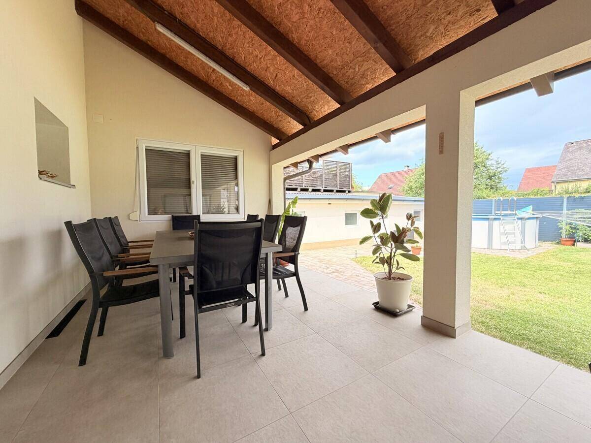 Überdachte Terrasse mit Esstisch und Stühlen, Blick auf den Garten und den Pool.