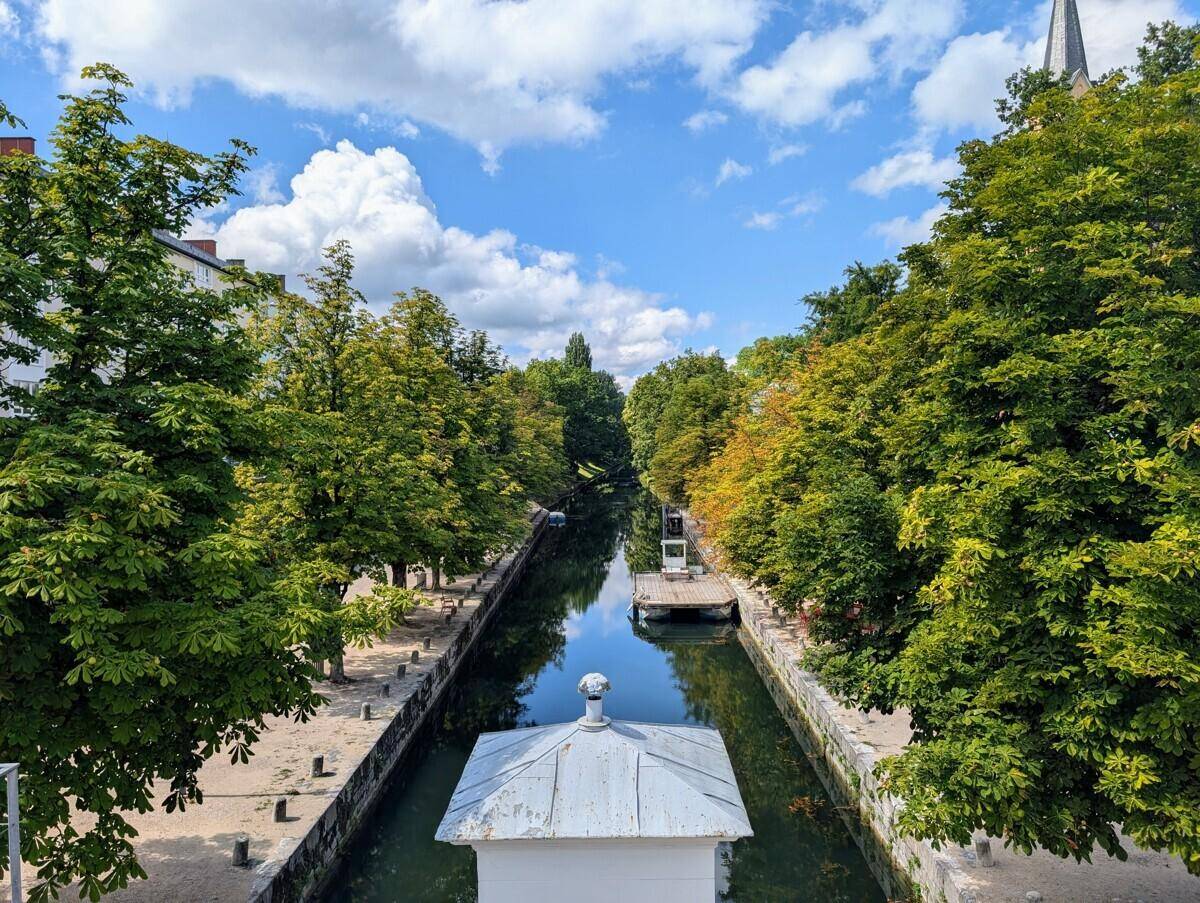 Kanal mit üppiger Baumallee und blauem Himmel, der sich durch die Landschaft schlängelt.