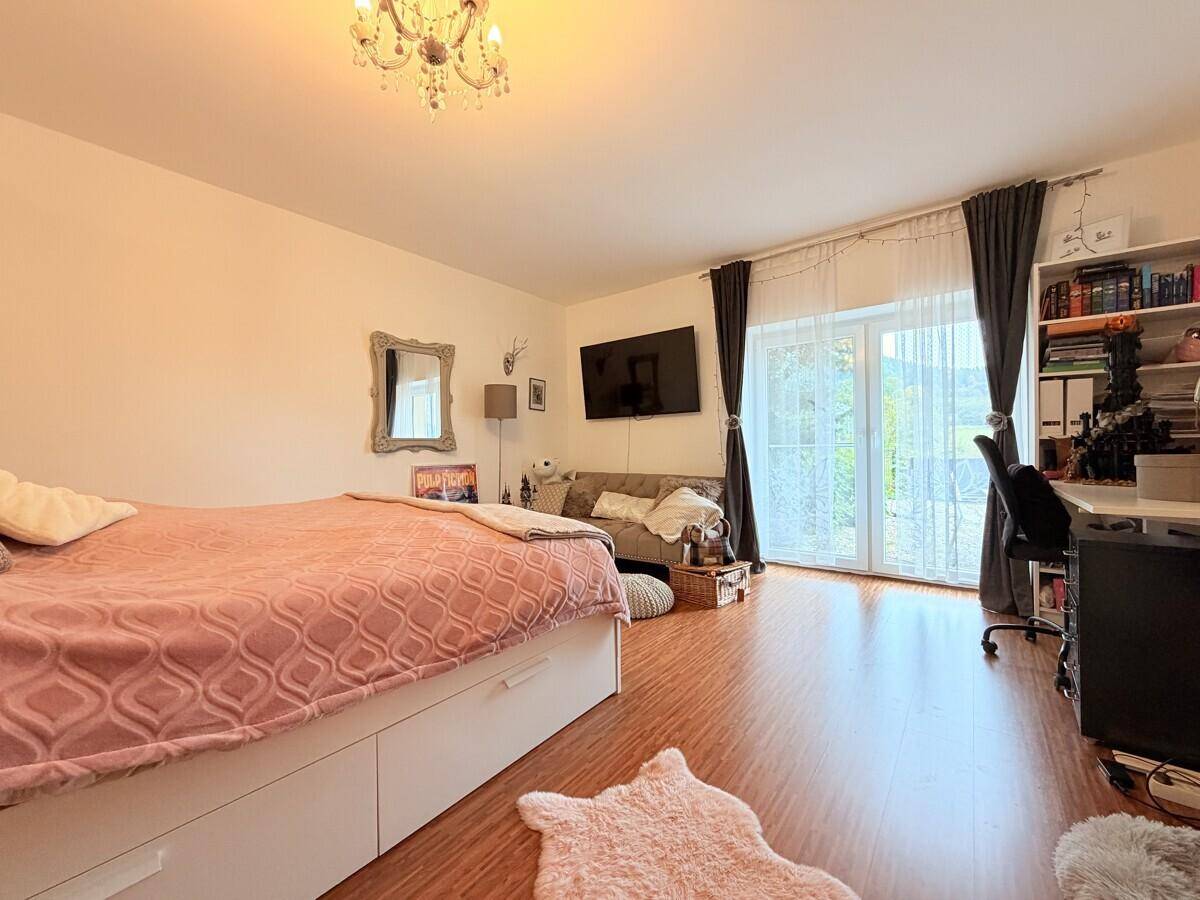 Helles Schlafzimmer mit Bett, Schreibtisch und Zugang zu einem Balkon.