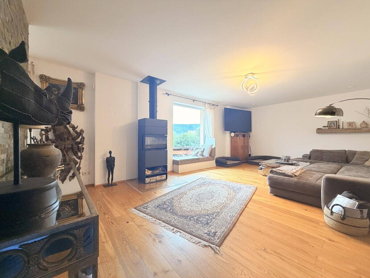 Helles Wohnzimmer mit Holzboden, Kaminofen und Blick auf die umliegende Landschaft.