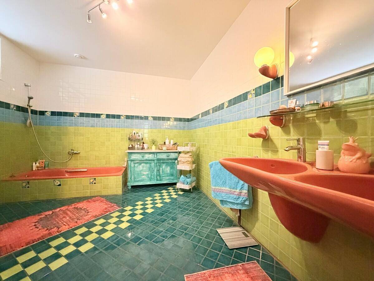 Farbenfrohes Badezimmer mit gelben und blauen Fliesen, roter Badewanne und Doppelwaschbecken.