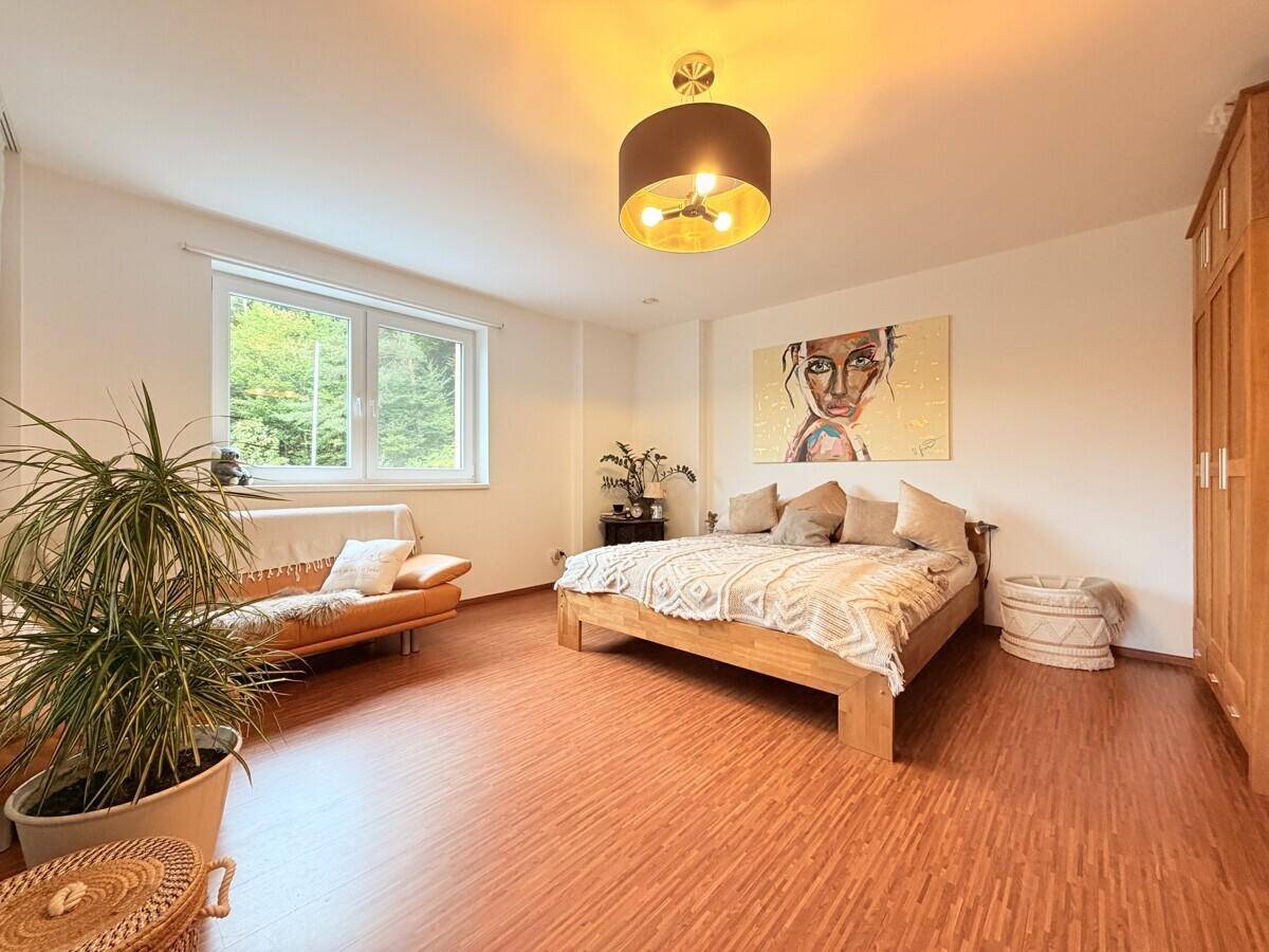 Gemütliches Schlafzimmer mit Holzbett, Pflanzen und großem Fenster zum Garten.
