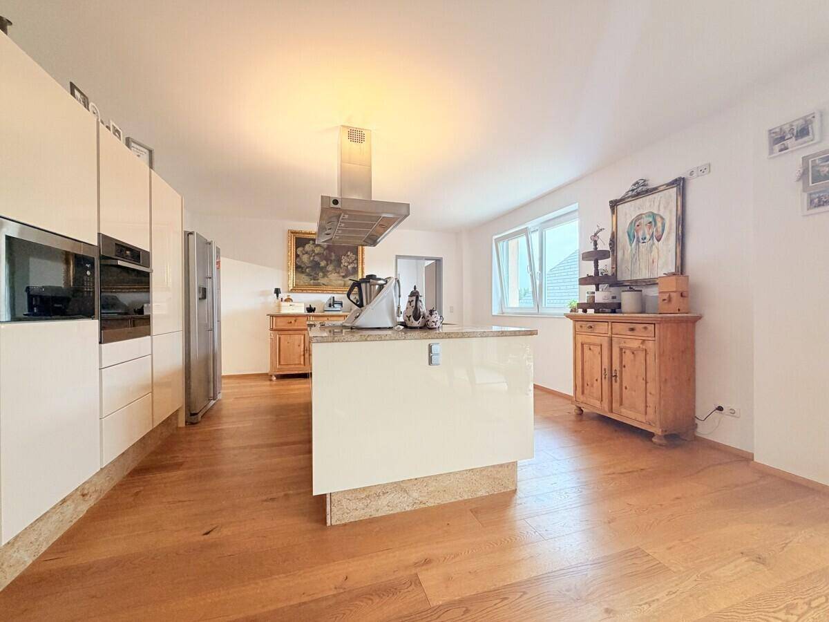 Moderne Küche mit weißer Hochglanzinsel, integrierten Geräten und Holzboden.