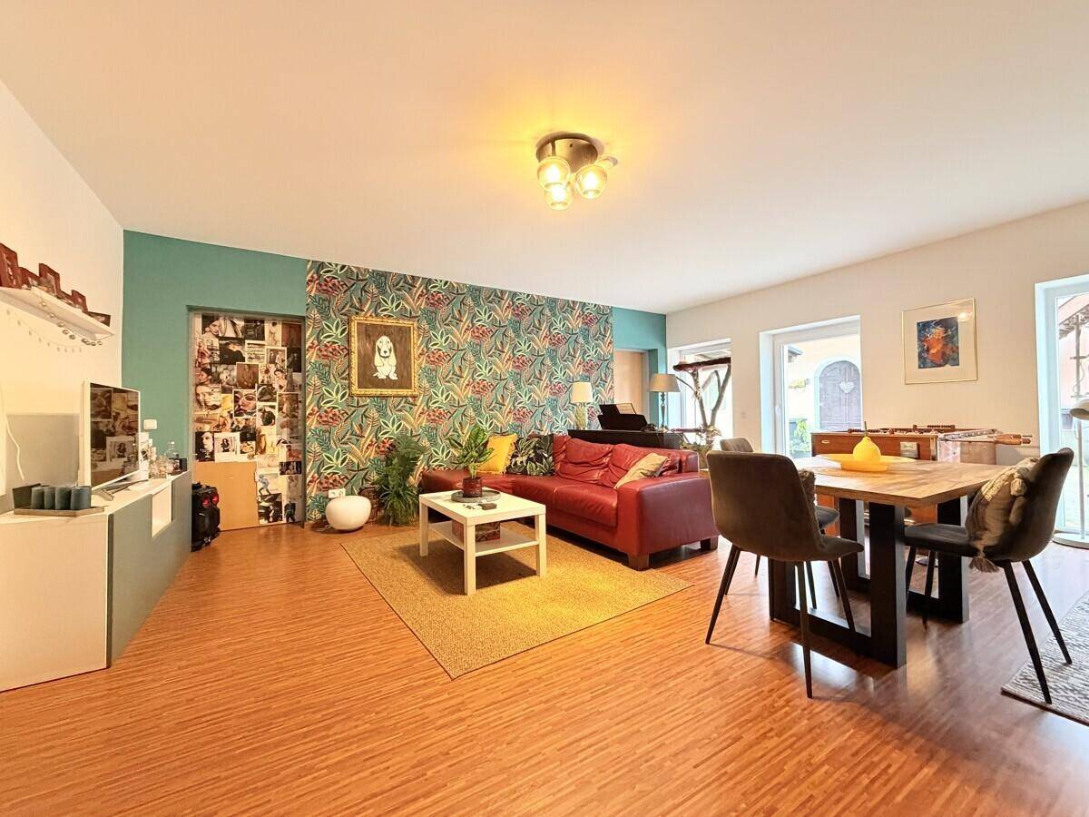 Offener Wohn-Essbereich mit rotem Sofa, Esstisch und dekorativer Tapete.