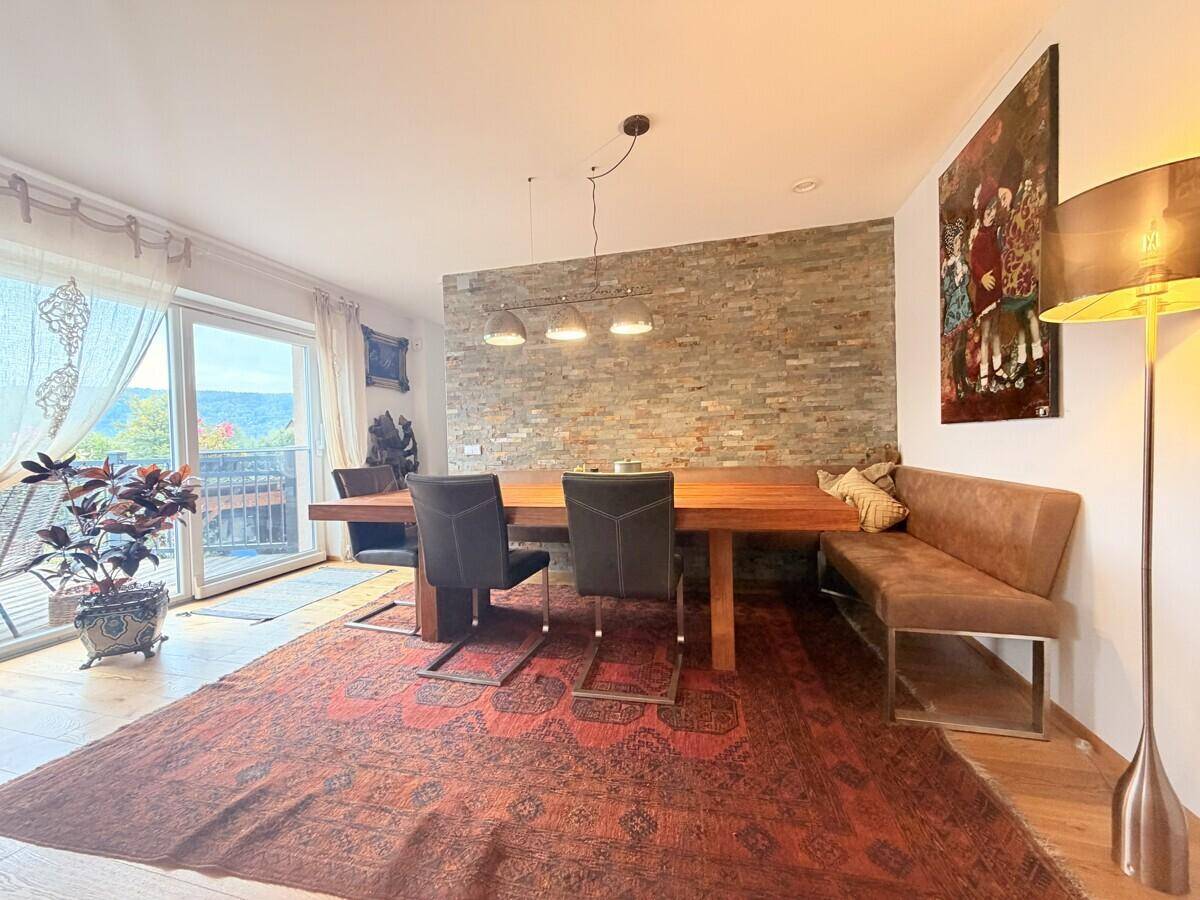 Gemütlicher Essbereich mit großem Holztisch, Steinwand und Zugang zu einem Balkon.