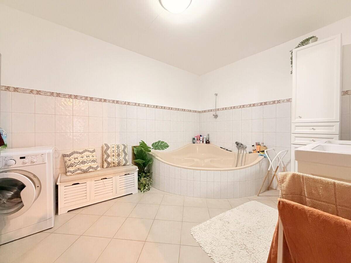Geräumiges Badezimmer mit Eckbadewanne, Waschmaschine und hellen Fliesen.