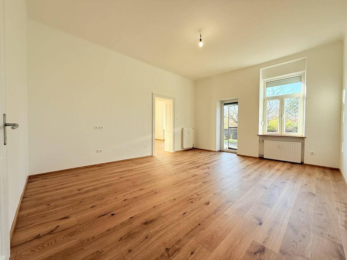Lichtdurchfluteter Raum mit Holzboden und Zugang zu einem Außenbereich durch eine Glastür.