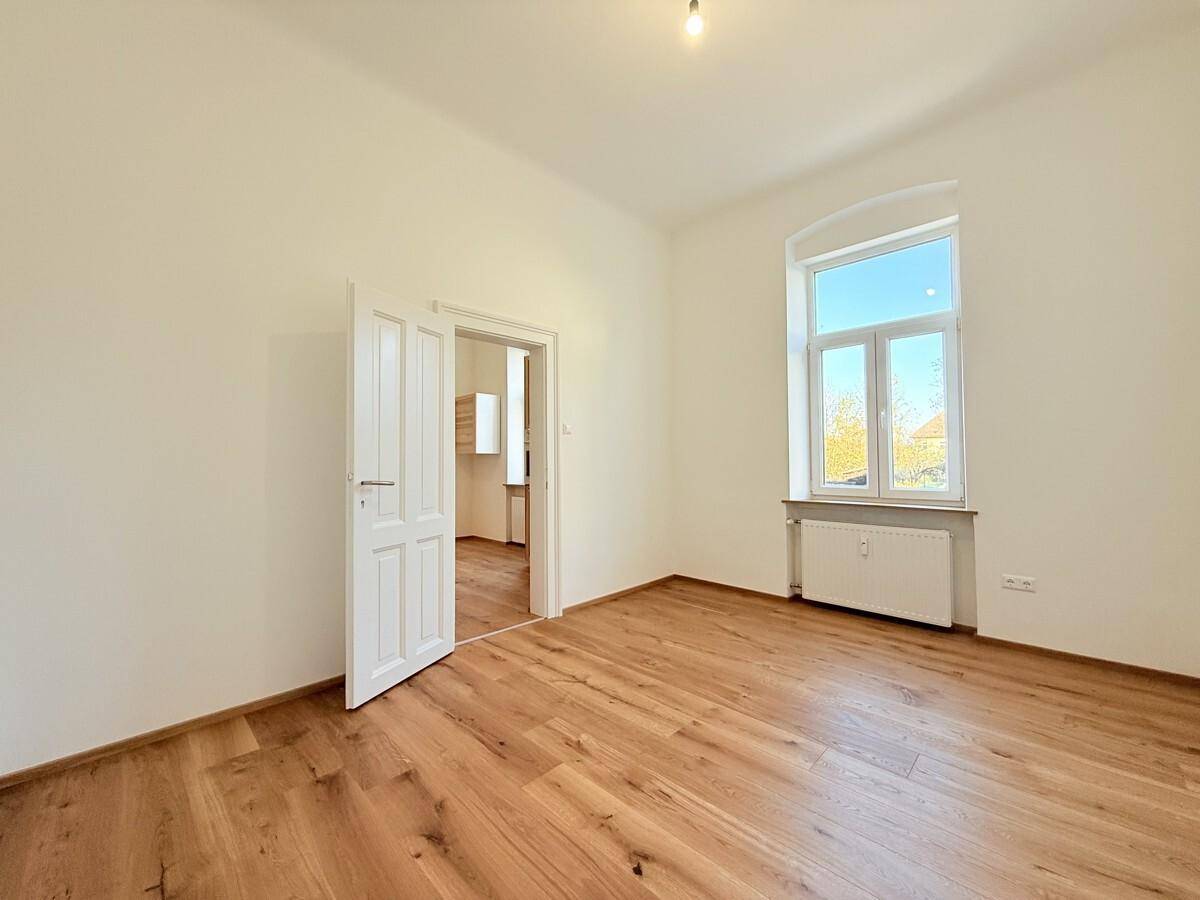Helles Wohnzimmer mit Eichenparkett und einem großen Fenster, das den Raum mit Tageslicht erfüllt.