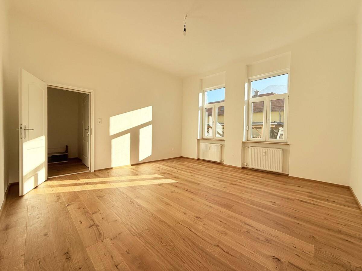 Helles, leeres Wohnzimmer mit neuem Eichenparkettboden und großen Fenstern, die viel Sonnenlicht hereinlassen.