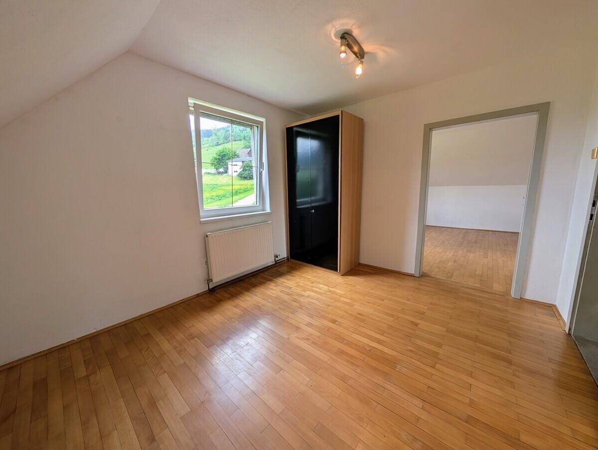 Freundliches Zimmer mit Holzparkett, Fenster und Kleiderschrank im Dachgeschoss.
