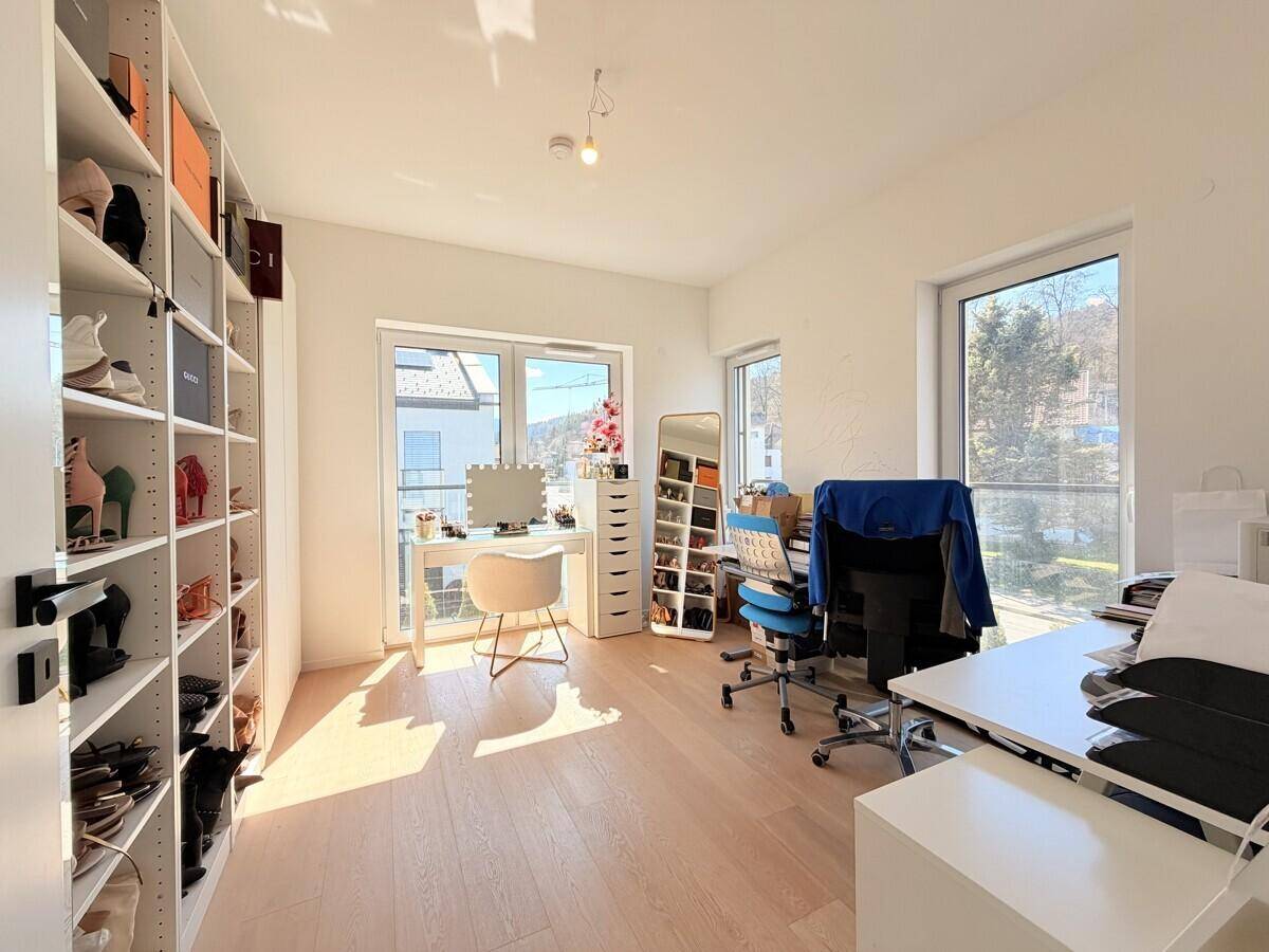 Vielseitiger Raum mit Schreibtischen, Regalen und großen Fenstern, ideal als Büro oder Ankleidezimmer.