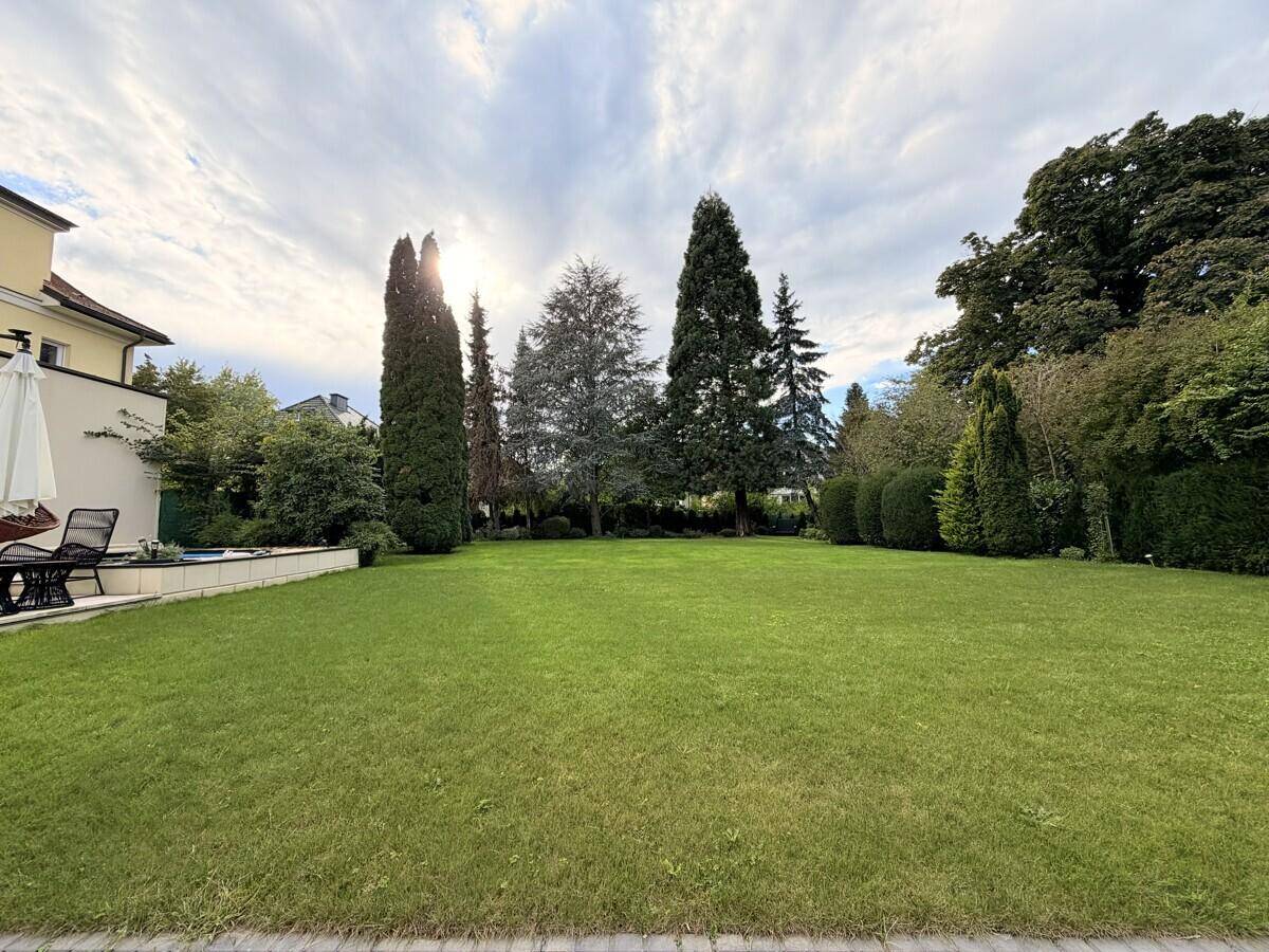 Weitläufiger Garten mit gepflegtem Rasen, hohen Bäumen und einem kleinen Poolbereich am Haus.